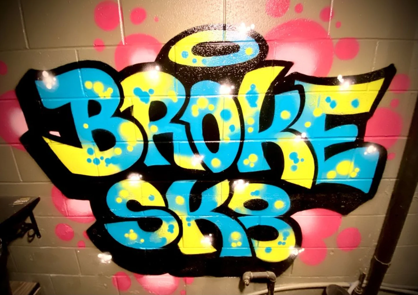 Blue and yellow Broke Sk8 bubble-letter graffiti with hot pink dots on a cinder block wall