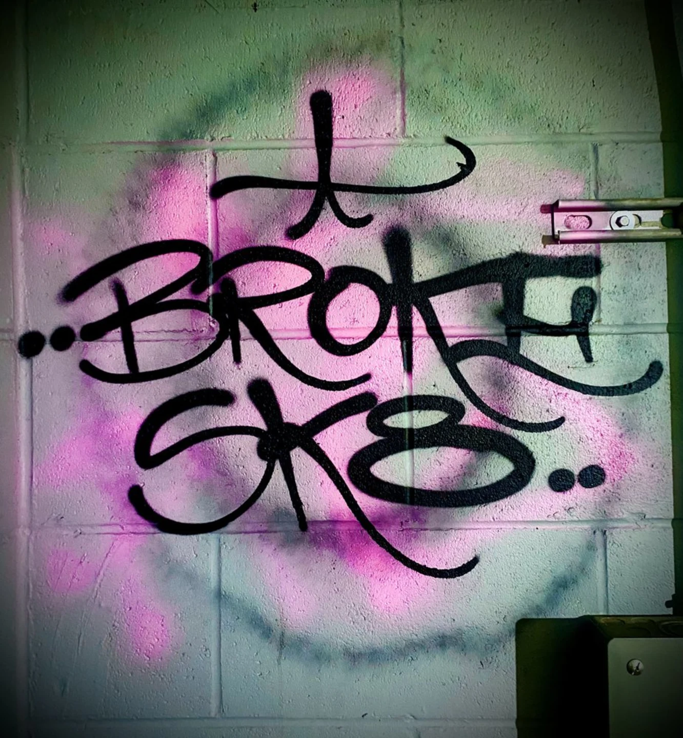 Black Broke Sk8 tag over pink and purple spray paint on the shop wall